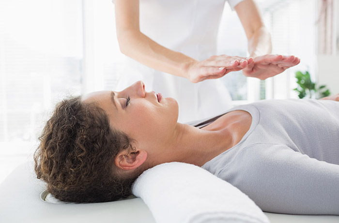 A woman is laying down and being given reiki.